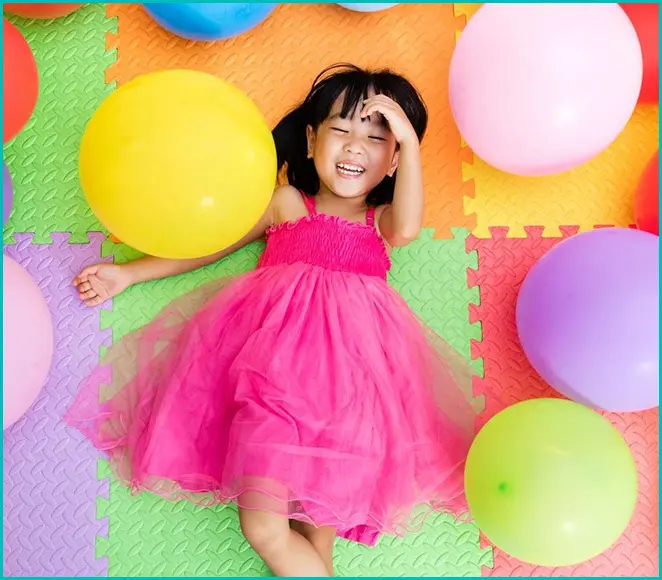 A little girl in pink dress laying on the ground with balloons.